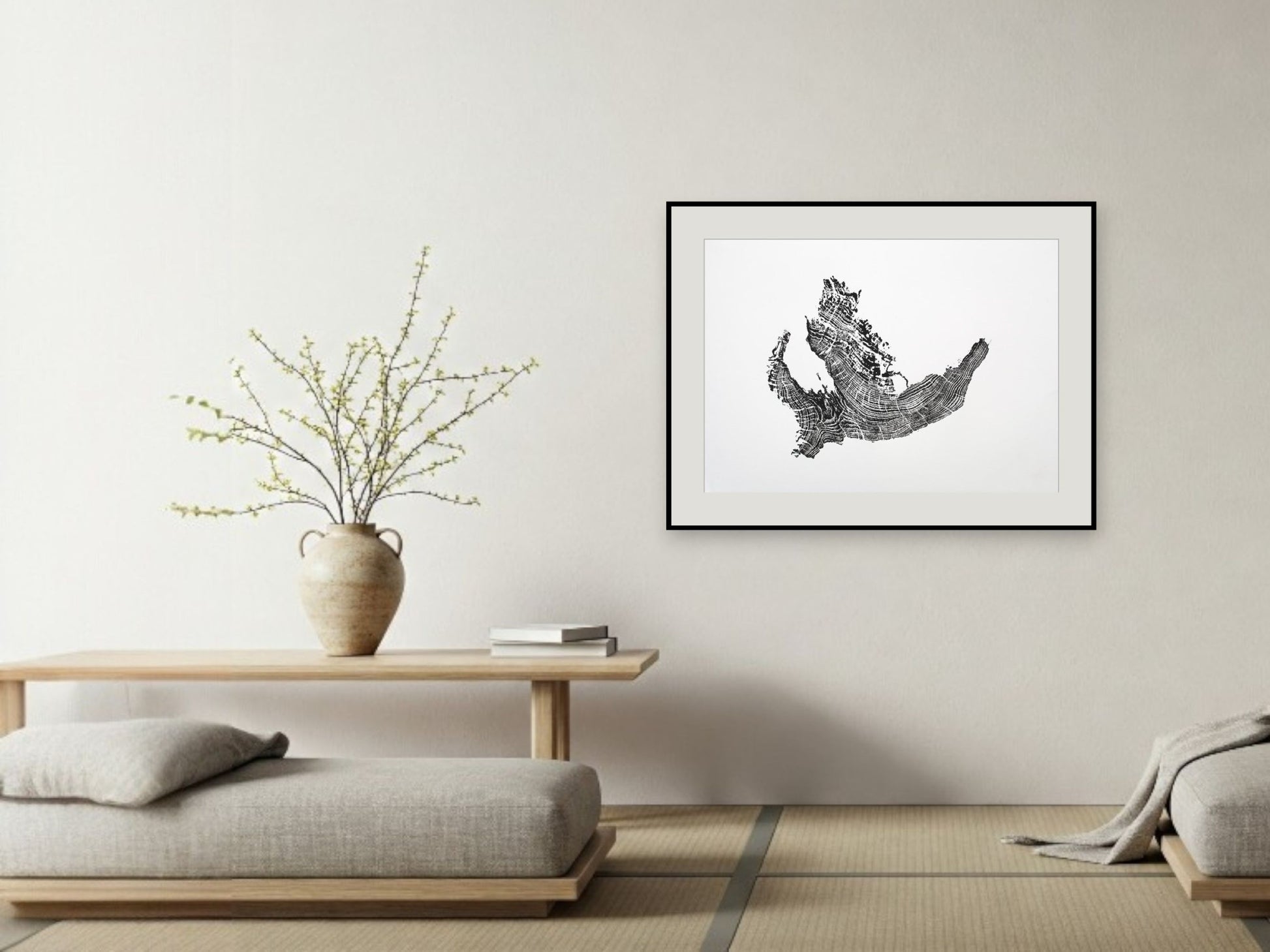 Framed black and white woodcut monoprint depicting an irregular tree root pattern on a white wall.